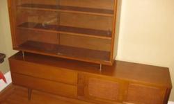 Here's an original mid-century wall unit/credenza/cabinet. Circa 1960s. It features a display area with for your glassware or collectibles, as well as drawers and a cabinet for storage. The shelves adjust. Its probably made of walnut or teak. In excellent