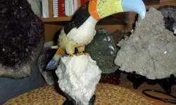 Natural Rock Gemstone Toucan Bird Sculpture Onyx Crystal. This handmade toucan was carved from hard-type rocks. The beautiful toucan stands on a calcite perch. The body was carved from travertine and onyx. The beak was carved from celestine, serpentine,
